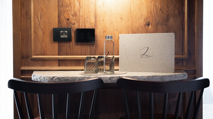 Moena, alberghi da sogno, panorama? C’è l’Hotel Latemar! Tavolo con due sedie, bottiglia d'acqua, due bicchieri e un menu su sfondo di legno