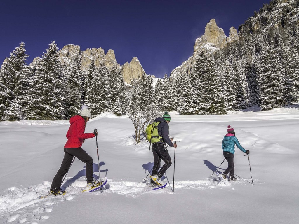 Passeggiate invernali in Val di Fassa: Hotel Latemar Tre persone fanno escursione con racchette da neve in montagna innevata