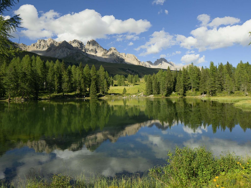 Val di Fassa: l’Hotel Latemar si trova qui Lago alpino tranquillo con riflessi di alberi e montagne soleggiate