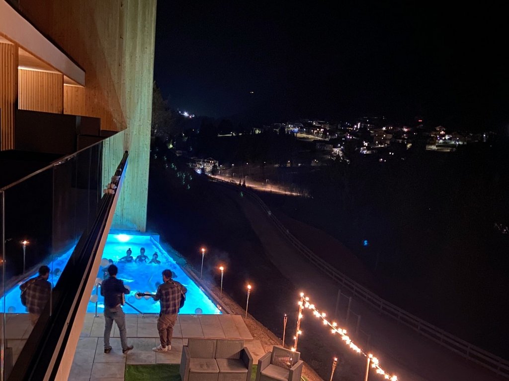 Dalla webcam il Latemar è bello, ma dal vivo è un sogno! Persone che suonano la chitarra vicino a una piscina illuminata di blu di notte