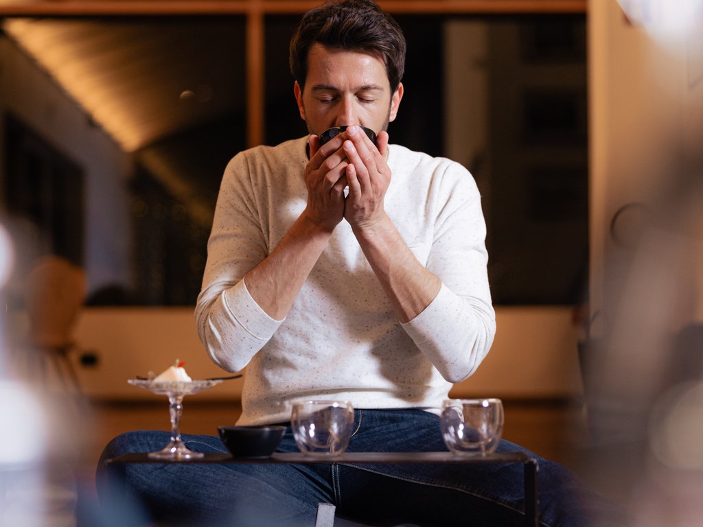 Val di Fassa e ciclabile: da ammirare dal cocktail & tea bar Uomo che beve da una tazza seduto a un tavolo basso in interni accoglienti