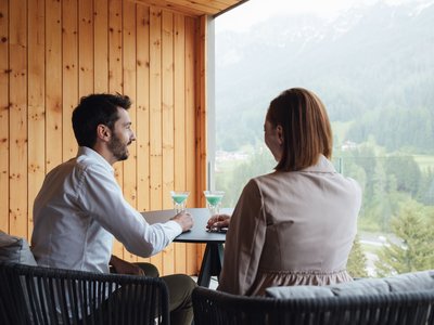 Escursioni da Moena e molto altro: il nostro programma Coppia che beve cocktail sul balcone con vista sulle montagne