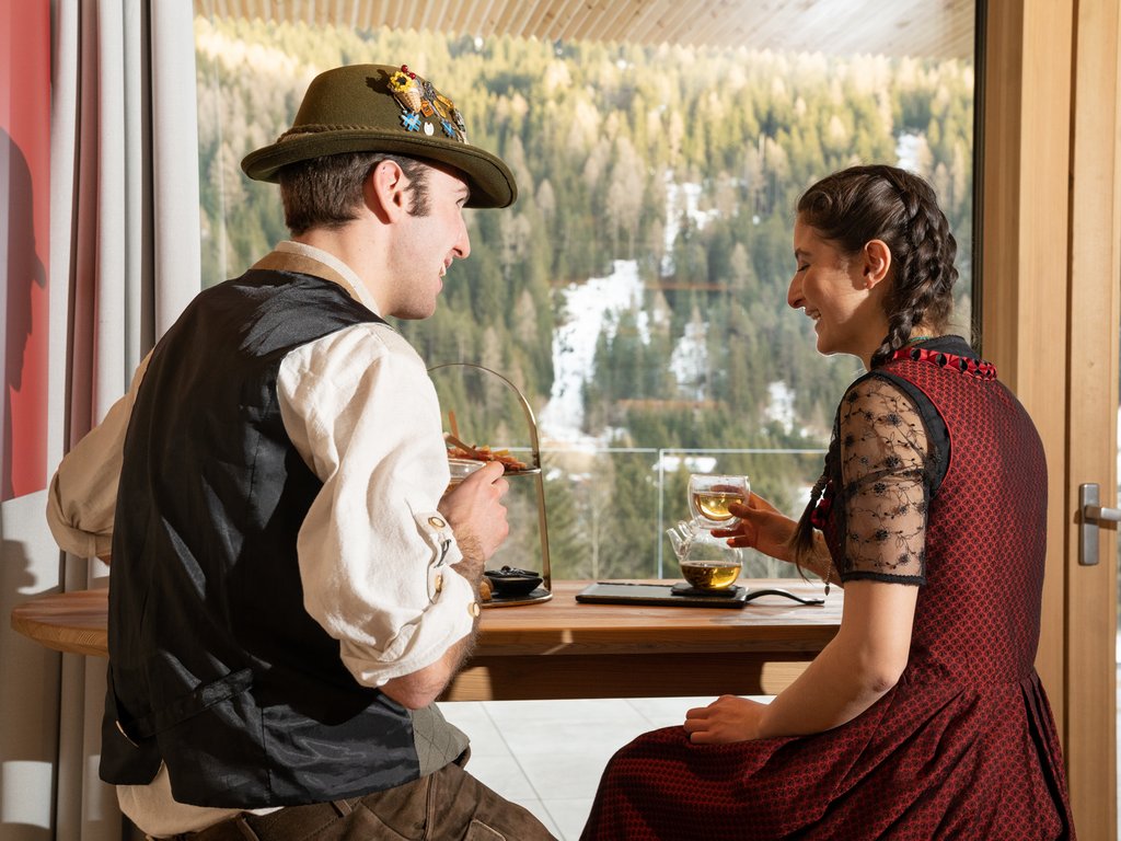Val di Fassa e ciclabile: da ammirare dal cocktail & tea bar Coppia in abiti tradizionali che beve tè con vista sulle montagne innevate