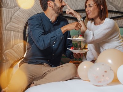 Escursioni da Moena e molto altro: il nostro programma Coppia che si diverte a scambiarsi dolci su un letto decorato con palloncini.