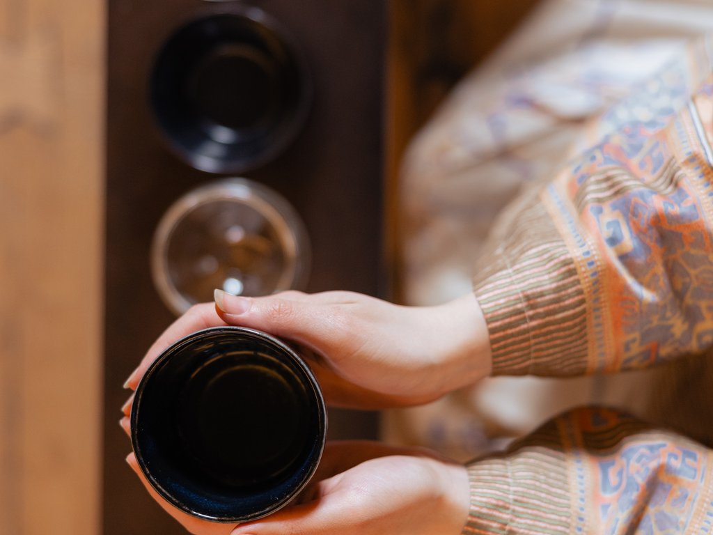 Val di Fassa e ciclabile: da ammirare dal cocktail & tea bar Mani che tengono una tazza nera sopra un tavolo con bicchieri