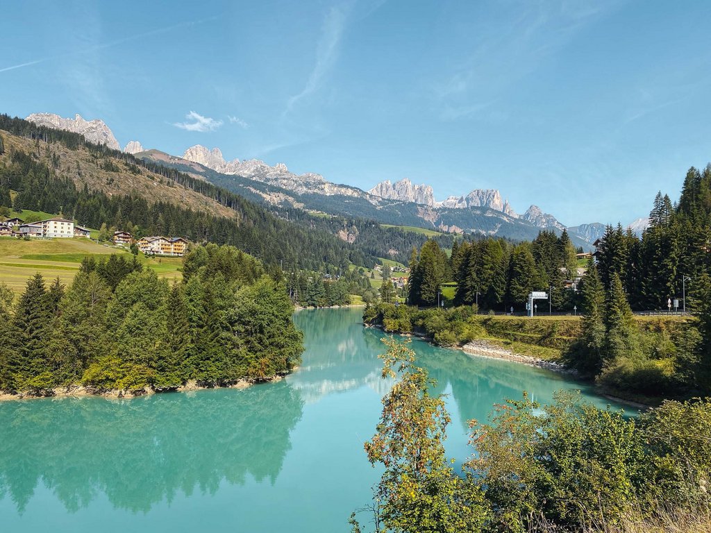 Hotel in Val di Fassa: il vostro Hotel Latemar Fiume azzurro con foresta e montagne sullo sfondo sotto un cielo sereno