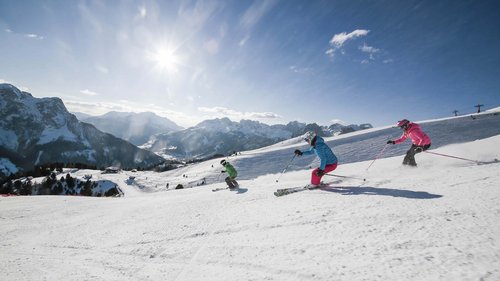 Hotel Latemar mit Dolomitenblick Drei Skifahrer fahren auf einer verschneiten Piste mit Bergen im Hintergrund