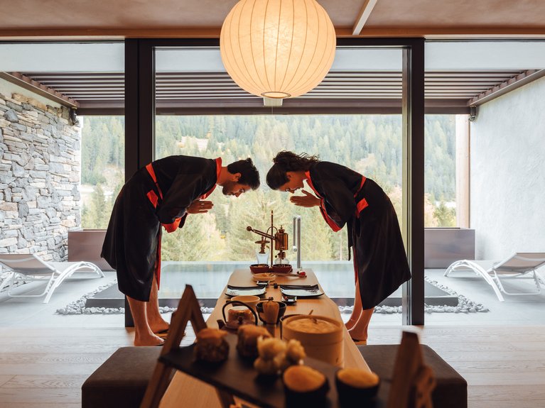 Val di Fassa in estate o inverno? Il relax non ha tempo! Coppia in kimono che si inchina durante una cerimonia del tè in una stanza con vista montagna