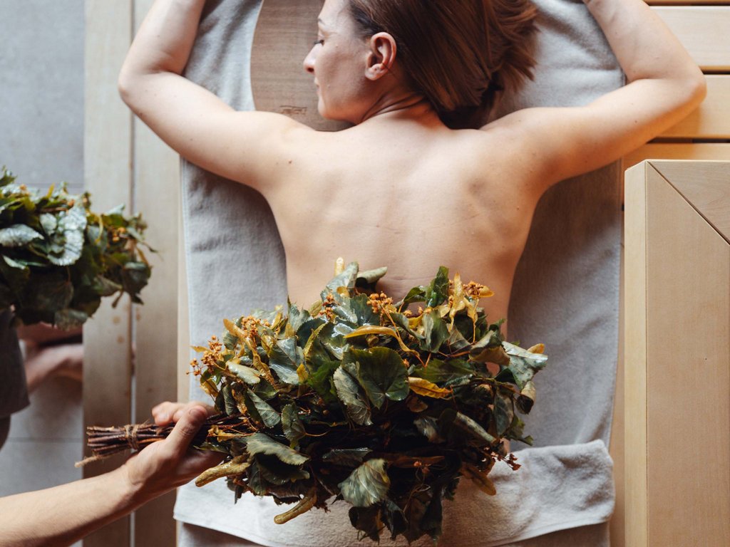 Al Latemar, dopo le passeggiate: relax nella Spa Oniro Donna sdraiata per massaggio con ramoscello di foglie su schiena