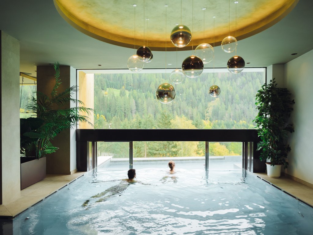 Soraga: dal lago alla piscina del Latemar Persone che nuotano in piscina interna con vista sulle montagne verdi