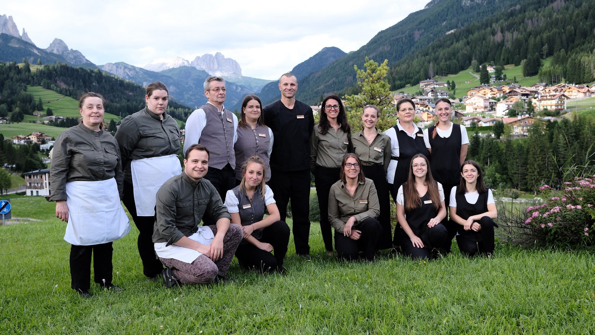 Vuoi entrare a far parte del nostro team? Gruppo di persone in divisa sul prato con vista montagna e villaggio