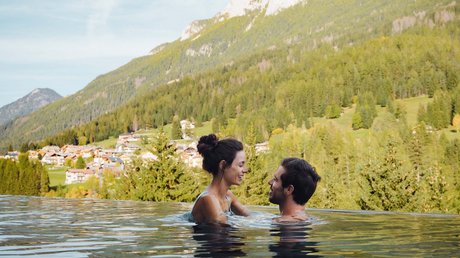 Meteo, Moena, Soraga, Latemar: tutto nella nostra gallery Coppia felice in piscina a sfioro con vista montagna e villaggio sotto cielo azzurro