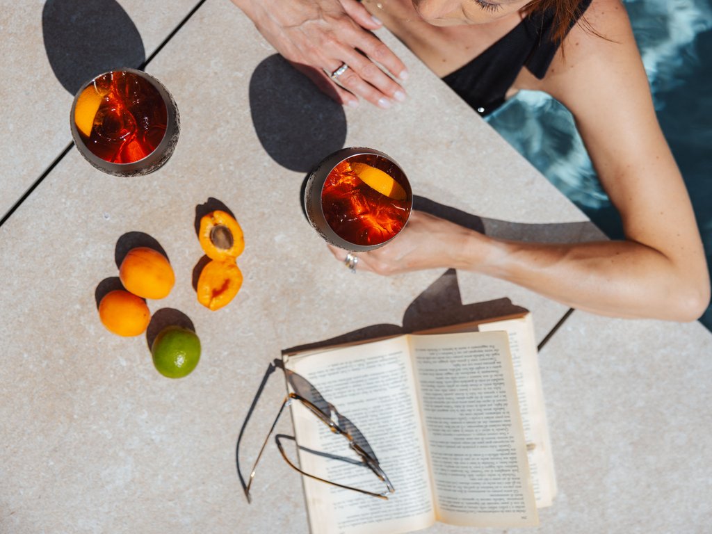A Soraga il meteo è sempre ottimo per un Day Spa! Donna in piscina con due cocktail, albicocche, lime e libro aperto con occhiali