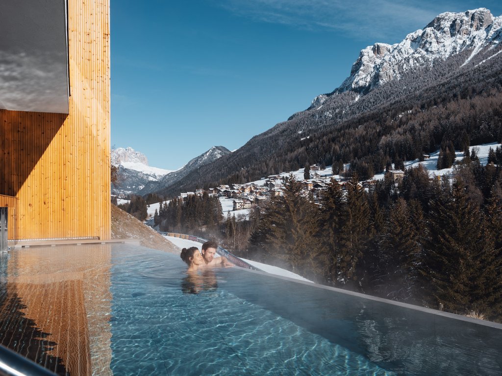 Soraga: dal lago alla piscina del Latemar Coppia in piscina riscaldata con vista sulle montagne innevate e villaggio