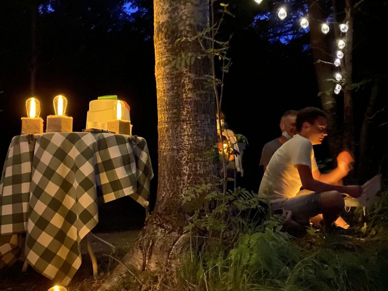 La pista ciclabile in Val di Fassa? C’è molto di più! Persone sedute vicino a un albero con luci decorative e lampade accese di sera
