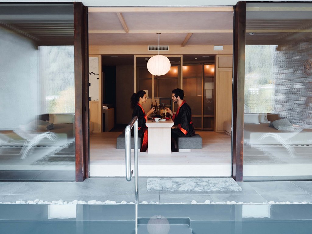 Hotel Latemar mit Dolomitenblick Paar in Kimonos isst in modernem Raum mit Pool davor