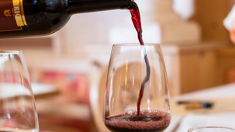 La pista ciclabile in Val di Fassa? C’è molto di più! Vino rosso versato da bottiglia in un calice su un tavolo apparecchiato