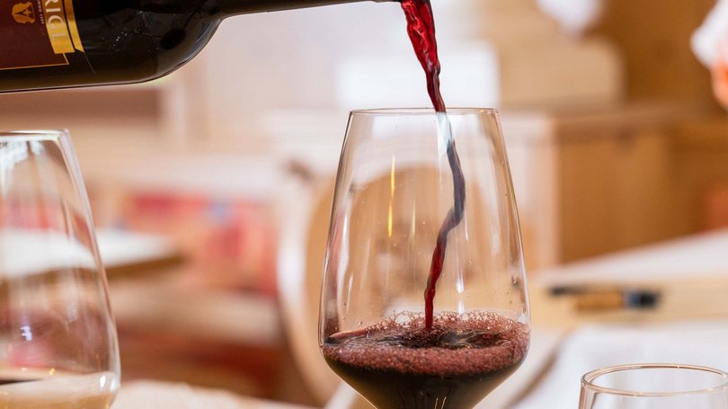 Escursioni da Moena e molto altro: il nostro programma Vino rosso versato da bottiglia in un calice su un tavolo apparecchiato