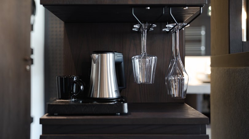 Moena, alberghi da sogno, panorama? C’è l’Hotel Latemar! Macchina per caffè con tazza nera e bicchieri appesi in una cucina scura