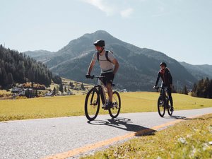Hotel in Val di Fassa: il vostro Hotel Latemar Due ciclisti su strada panoramica nella campagna con montagne sullo sfondo