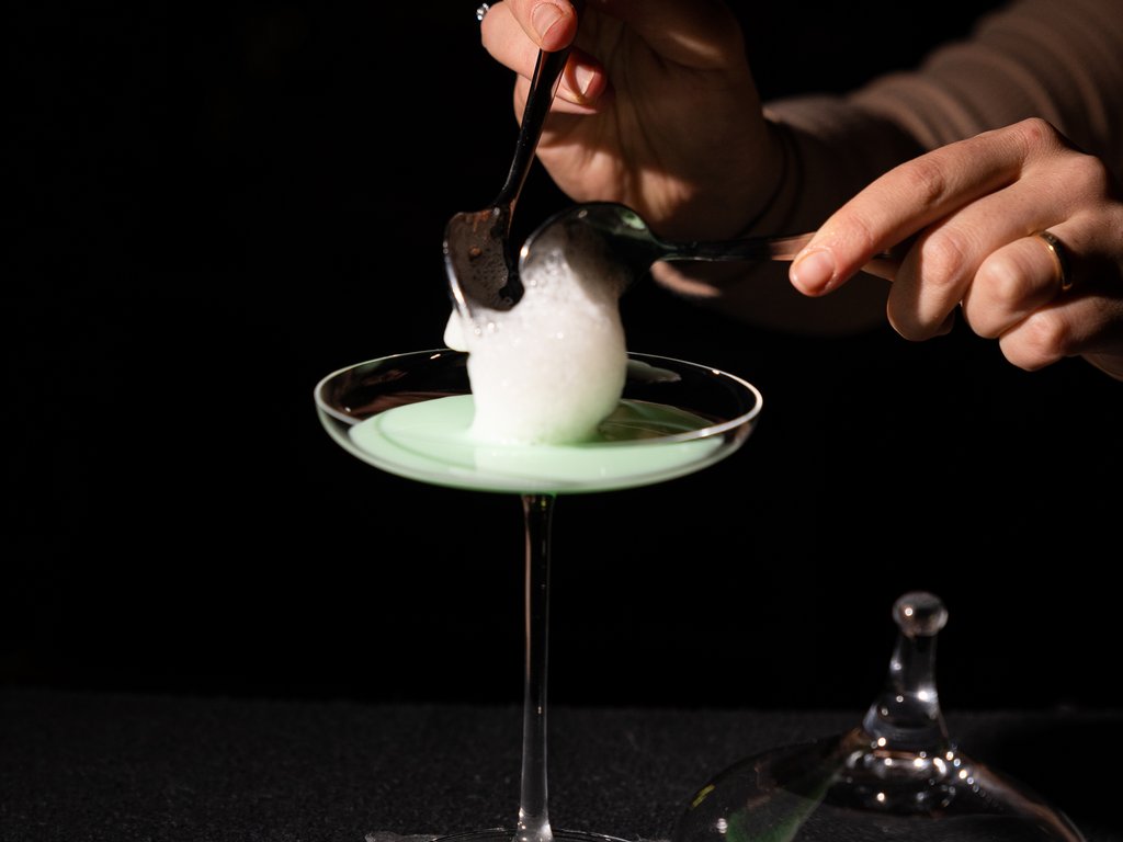 Val di Fassa e ciclabile: da ammirare dal cocktail & tea bar Mano che aggiunge schiuma sopra un cocktail verde in un bicchiere da cocktail