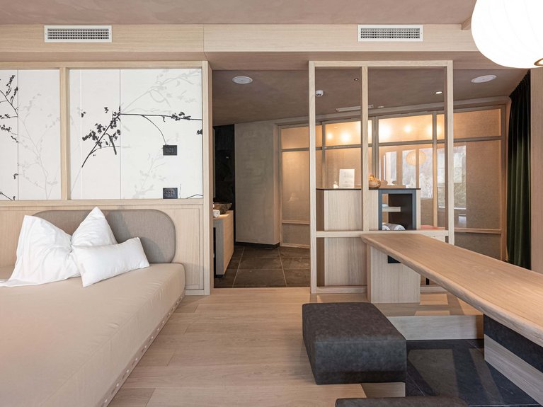 Val di Fassa in estate o inverno? Il relax non ha tempo! Interno di soggiorno moderno con divano, tavolo in legno e parete divisoria