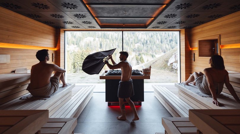Escursioni da Moena e molto altro: il nostro programma Interno di sauna moderna con tre persone avvolte in asciugamani