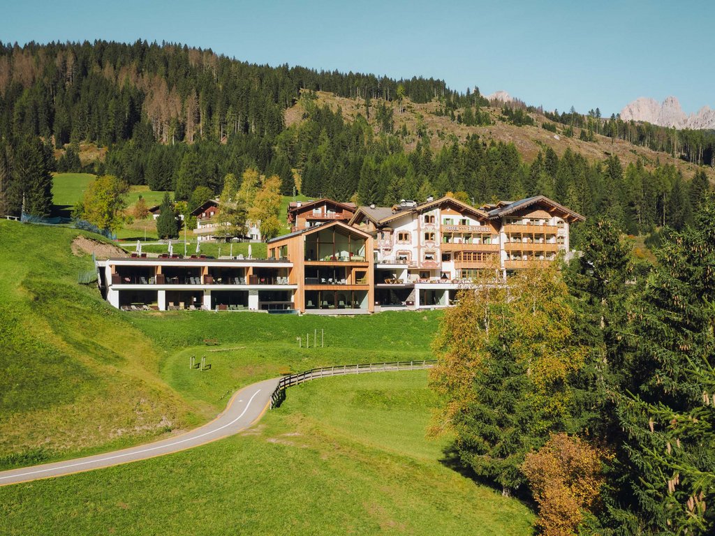 Val di Fassa: dove dormire e vivere vacanze sostenibili Hotel in stile alpino circondato da prati verdi e boschi in montagna