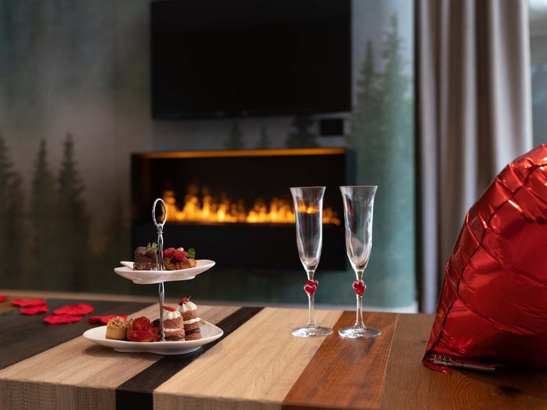 Hotel Latemar con vista sulle Dolomiti Tavolo con dolci, due bicchieri e palloncino rosso a forma di cuore davanti a camino acceso
