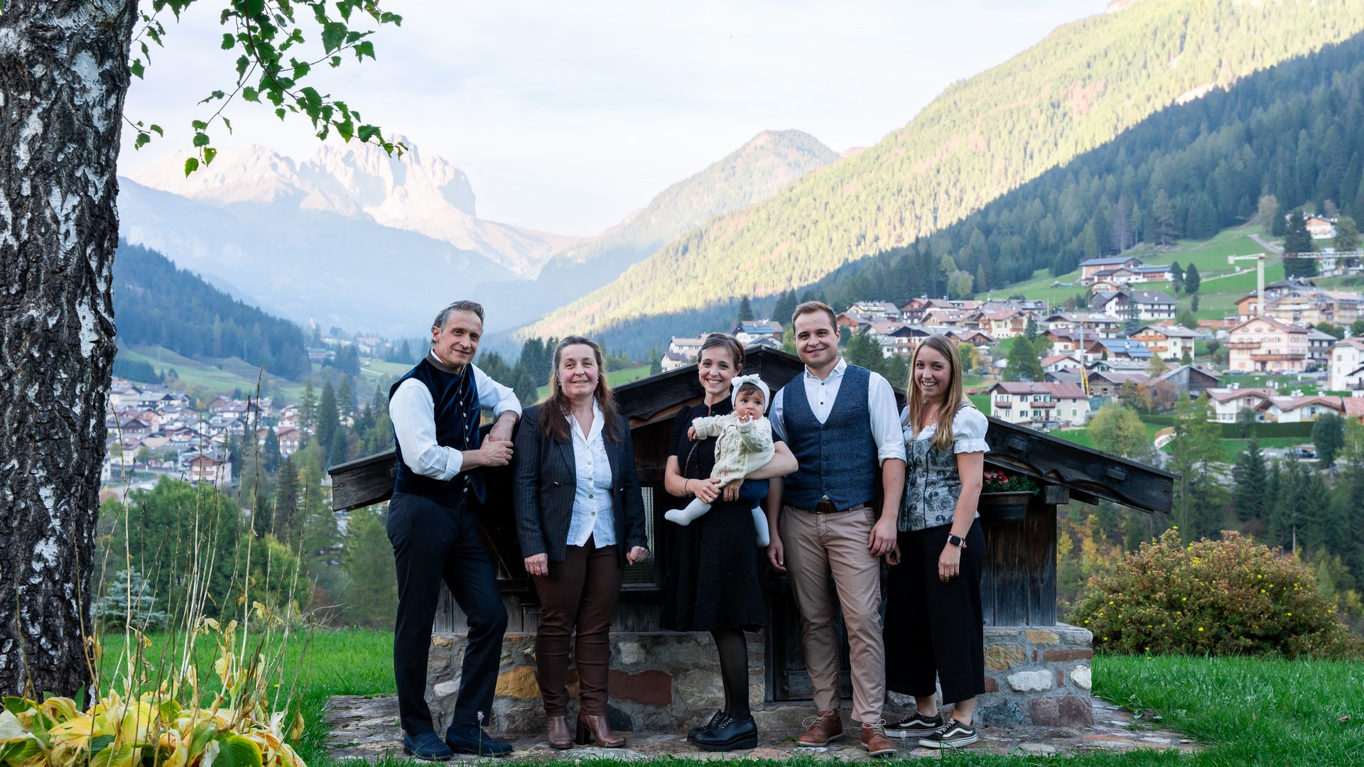 Hotel in Soraga: family passion Group of six people in traditional clothes with mountain village background