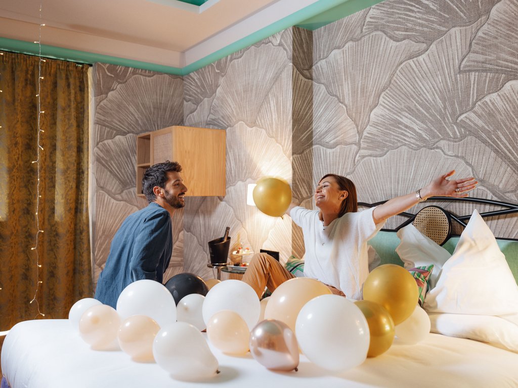 On the cycle track, from Moena to your romantic oasis Happy couple playing with balloons on large bed in bedroom.