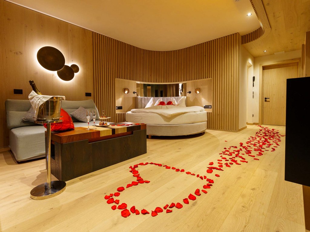 On the cycle track, from Moena to your romantic oasis Romantic room with heart-shaped rose petals, round bed, and champagne