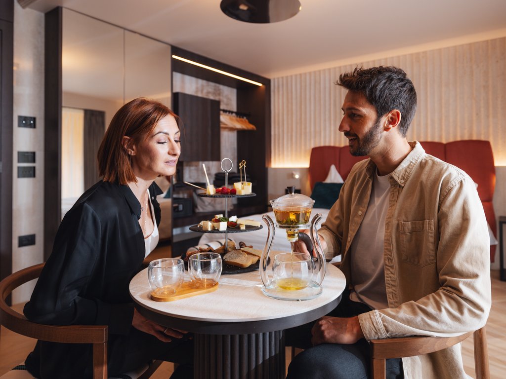On the cycle track, from Moena to your romantic oasis Couple enjoying tea and snacks at a round table in a modern room.