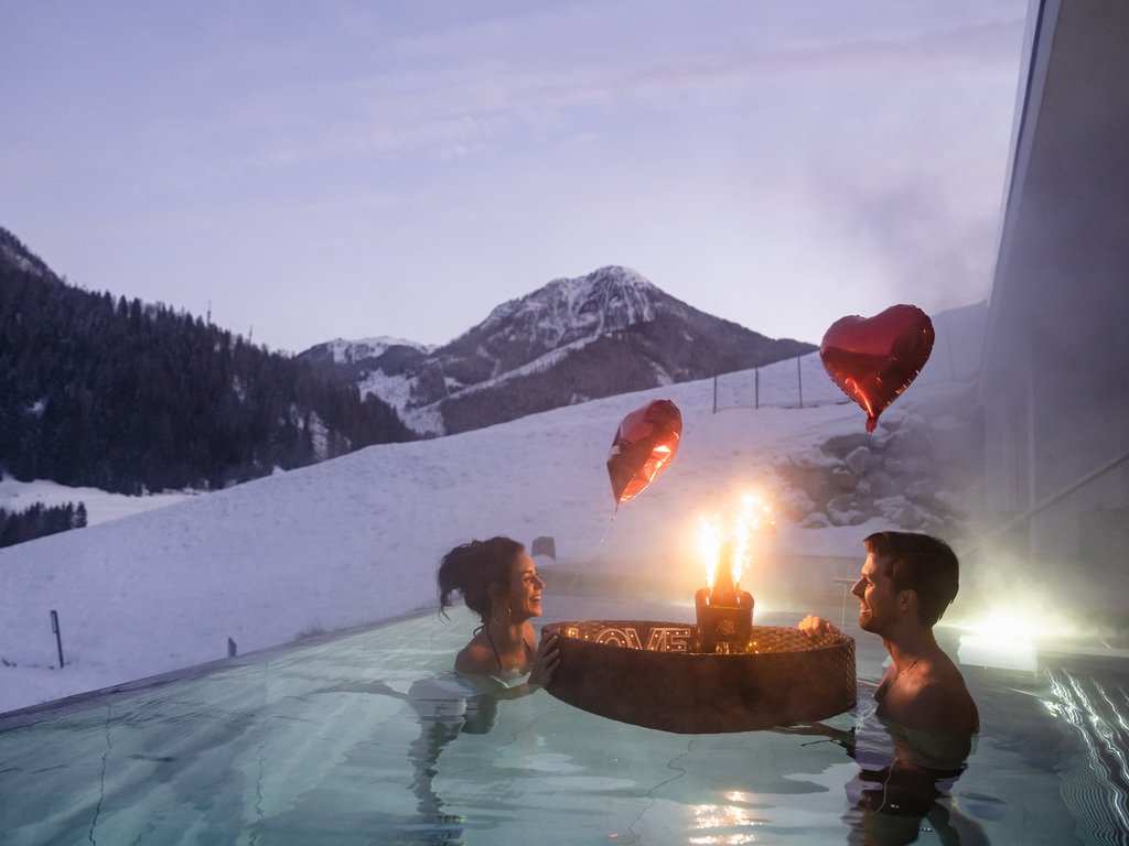 On the cycle track, from Moena to your romantic oasis Couple enjoying romantic evening in outdoor hot tub with heart balloons by snowy mountains