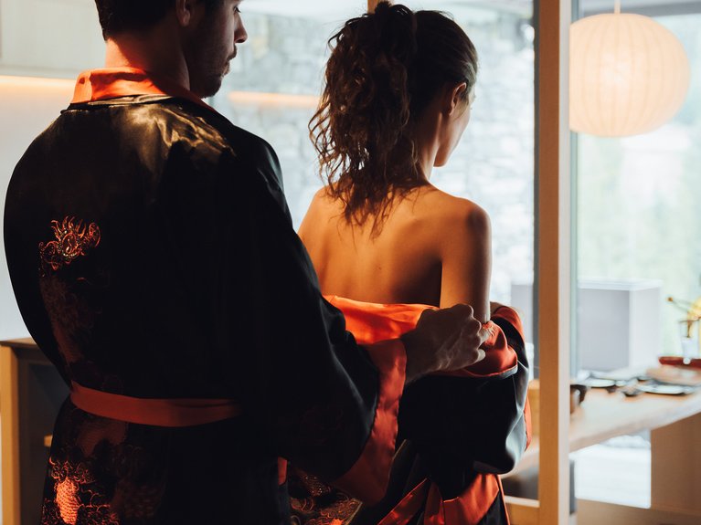 On the cycle track, from Moena to your romantic oasis Man helping woman put on a black and red robe in a modern room