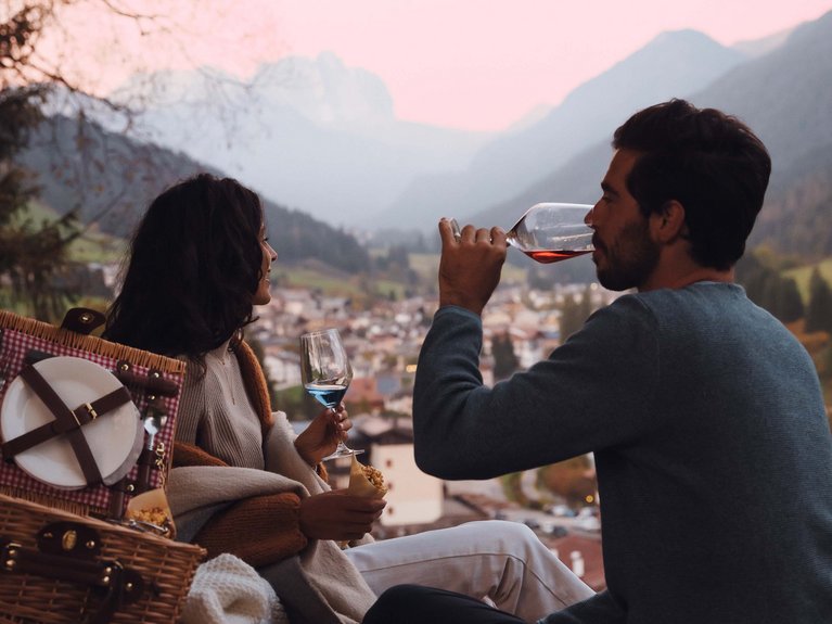 On the cycle track, from Moena to your romantic oasis Couple having picnic with wine and food in the mountains at sunset