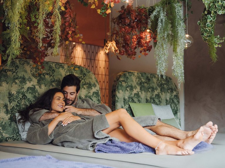 On the cycle track, from Moena to your romantic oasis Couple in robes embracing and relaxing in room with hanging plants