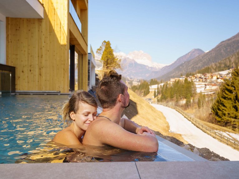 On the cycle track, from Moena to your romantic oasis Couple relaxing in pool overlooking snowy mountain landscape